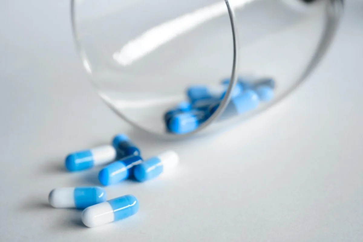 Blue and white capsules spilling from a tipped drinking glass.