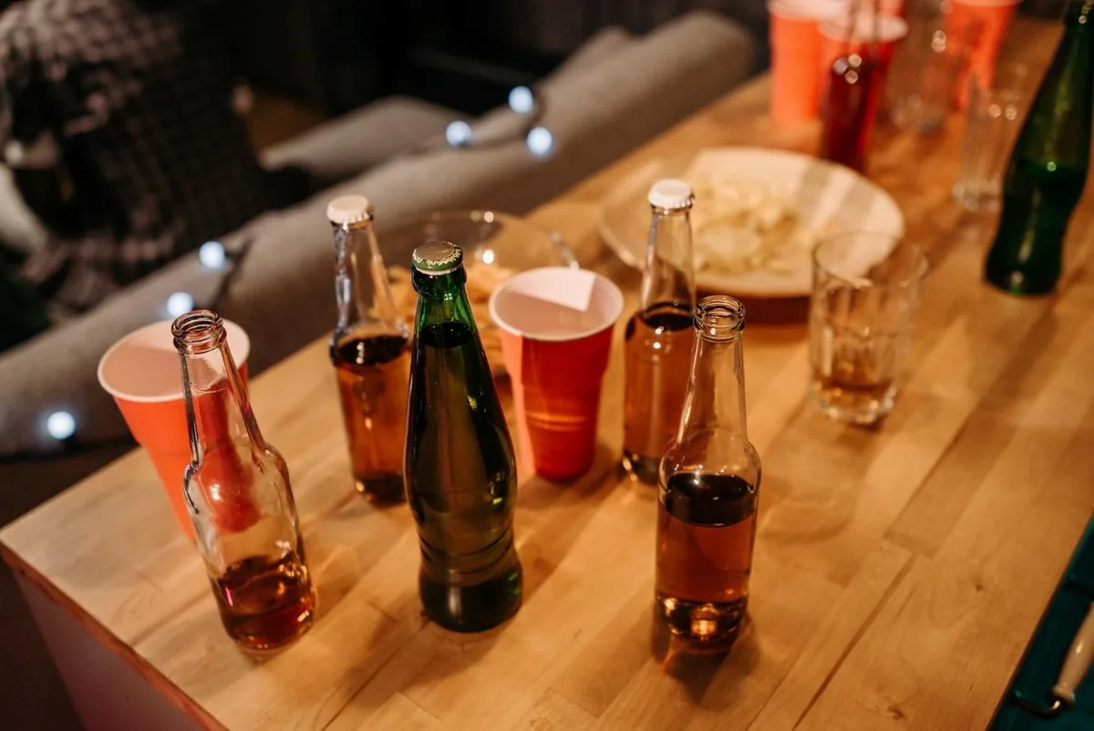 Bottles and plastic cups of alcohol crowded together on a table.